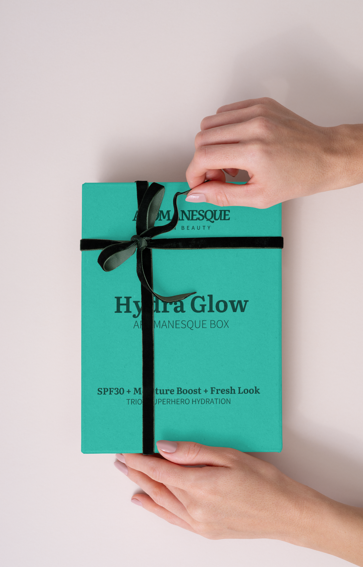 A hand holding a turquoise skincare product called 'Aromanesque Hydra-Glow' which includes sunscreen, hydration gel, and eye cream. 