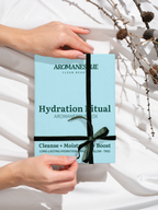 A hand holding a blue spa-like product box with 'Aromanesque' branding and the words 'Hydration Ritual - Cleanse, Moisturize, Boost' on it, with a decorative bow on the front.