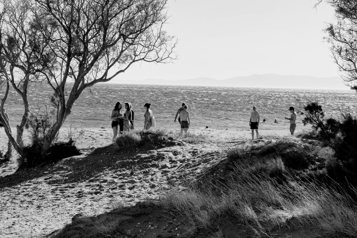 Aromanesque - Black and white photo of people on a beach with trees and sand dunes.